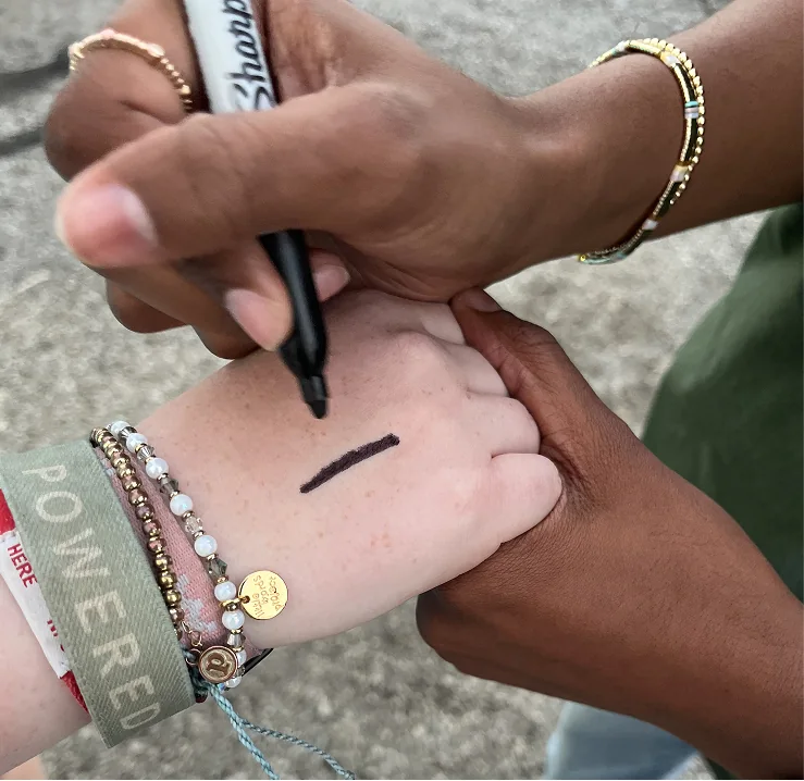 One person drawing the A Third of Us line on another's hand with a marker