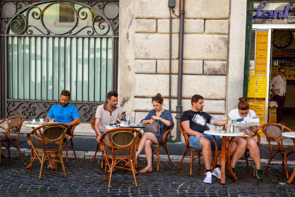 Diverse group of young adults reading and discussing outside a cafe in an urban setting.