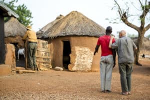 Traditional African village scene with two men walking towards a thatched hut.