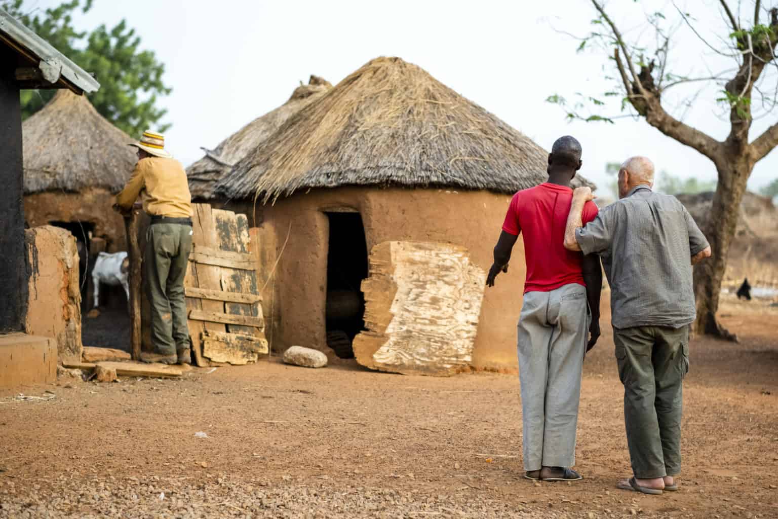 Traditional African village scene with two men walking towards a thatched hut.