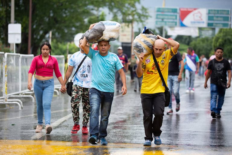 Refugees carrying belongings in the rain, highlighting resilience and recovery from trauma.
