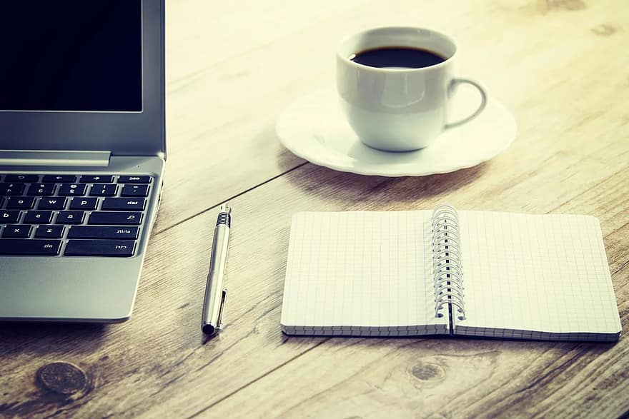 Workspace with laptop, notebook, pen, and coffee for strategic planning.