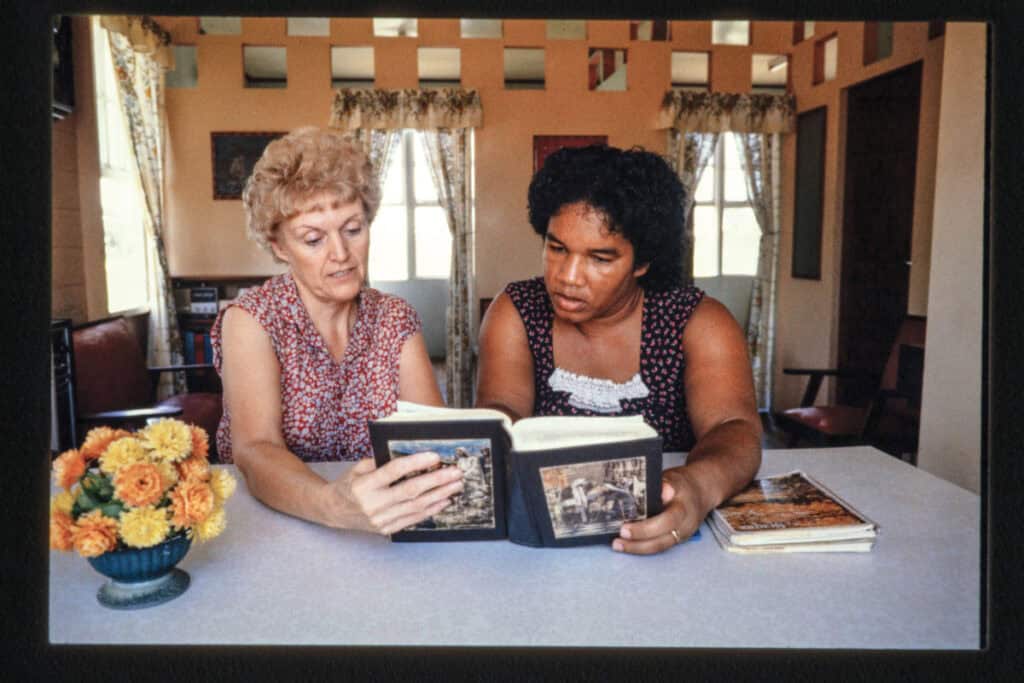 Two women looking at photo albums at a table in a cozy room.