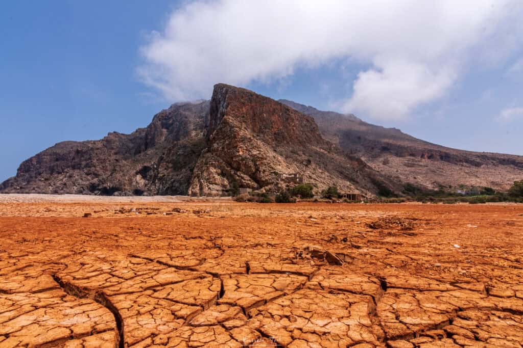 Dry cracked earth with mountain in the background, symbolizing climate change impacts.