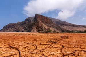 Dry cracked earth with mountain in the background, symbolizing climate change impacts.