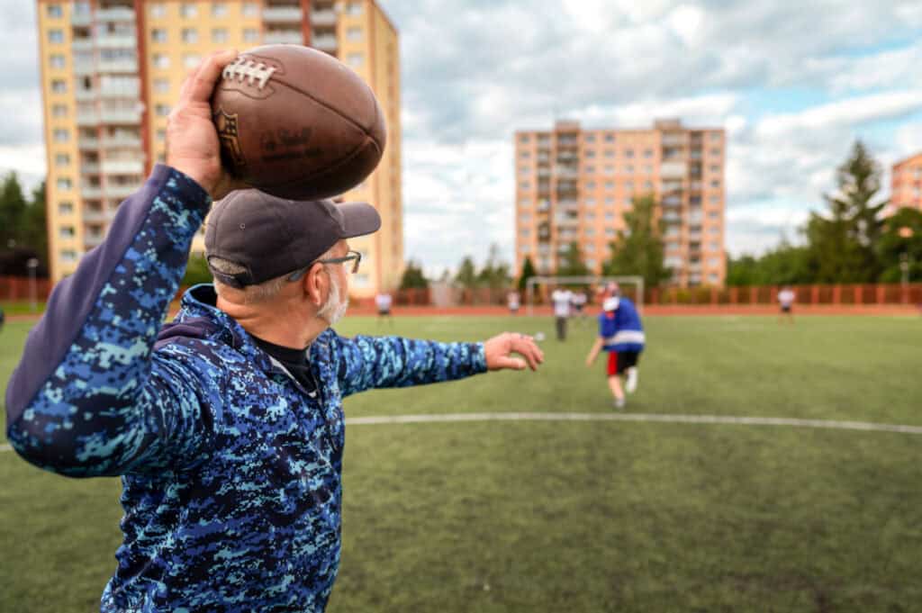 Football coach with a ball ready to throw during practice on a sports field.