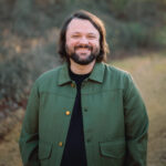 Man smiling outdoors with trees in background, representing healthy missions agencies.