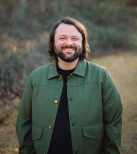 Man smiling outdoors with trees in background, representing healthy missions agencies.