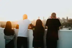 Group of diverse young adults watching sunset over city skyline from rooftop.