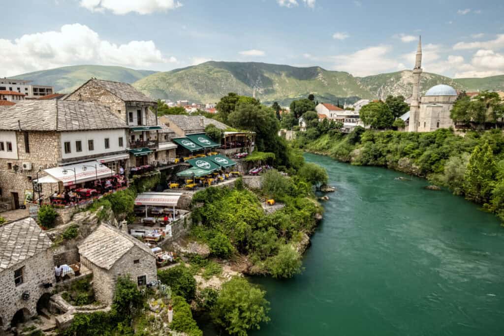 Scenic view of a riverside town with historic buildings and mountains in the background.