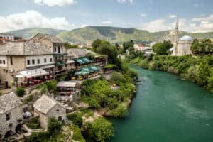 Scenic view of a riverside town with historic buildings and mountains in the background.