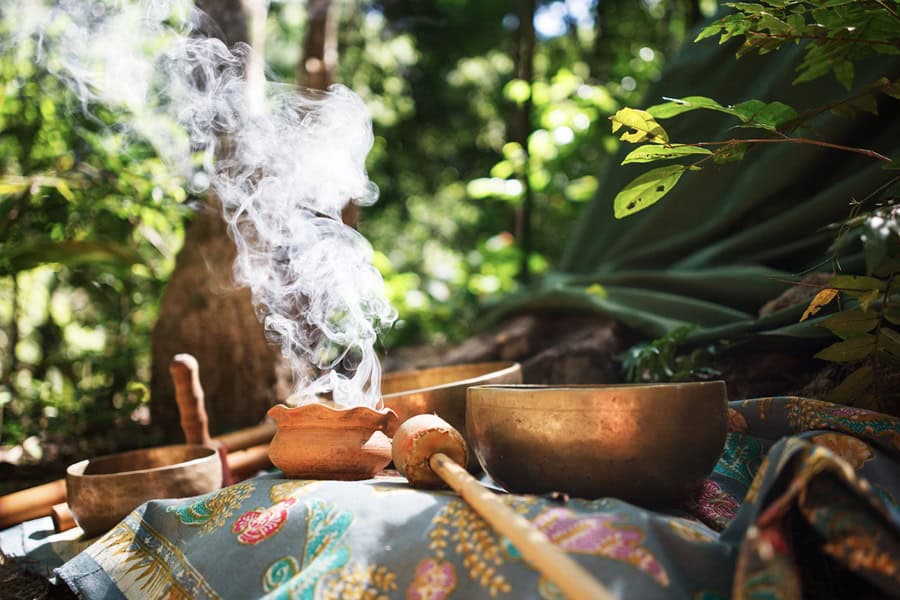 Traditional prayer instruments and incense in a lush outdoor setting.