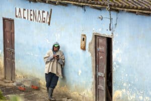 Woman standing outside a blue building using a mobile phone in a rural setting.