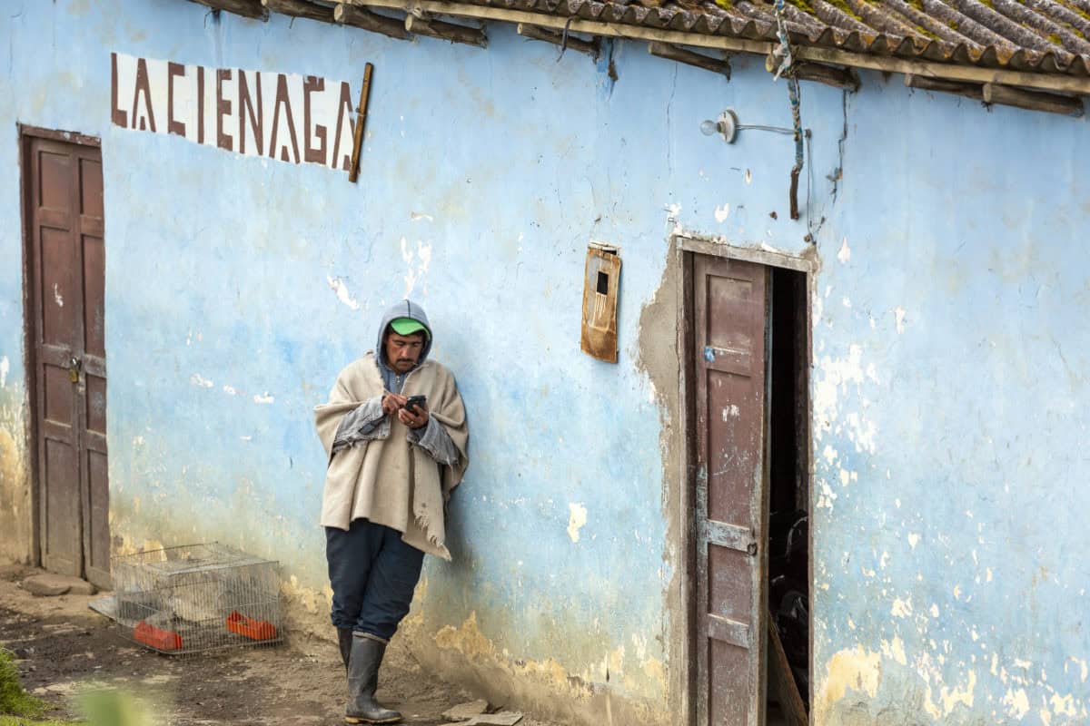 Woman standing outside a blue building using a mobile phone in a rural setting.