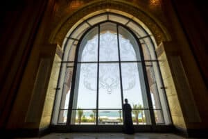 Person looking out large arched window with ocean view and decorative design.