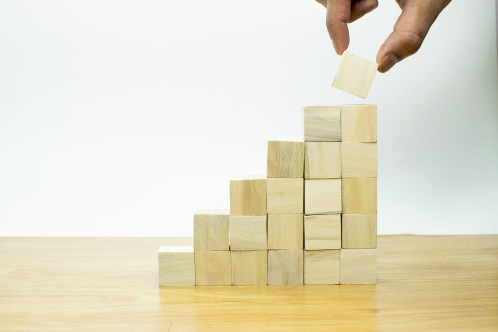 Hand stacking wooden blocks to symbolize growth and progress in ministry.