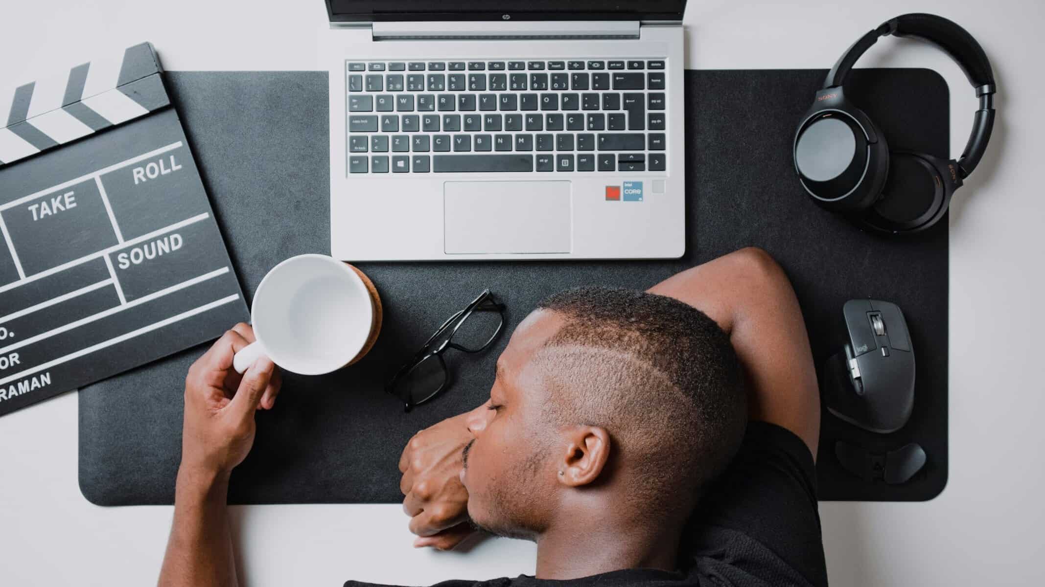 Young man resting at a workspace with laptop, headphones, and film clapperboard.